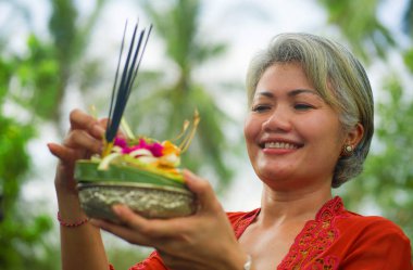 Bali Tapınağı 'nda elinde tütsü çubuğu ve çiçek sunan geleneksel Bali dini geleneği giymiş güzel ve mutlu Asyalı kadın. 
