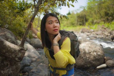 Genç, güzel ve mutlu Asyalı kadın sırt çantasıyla dağları aşarak nehri geçiyor. Tatil doğasının tadını çıkarıyor ve neşeli bir yürüyüş yapıyor. 