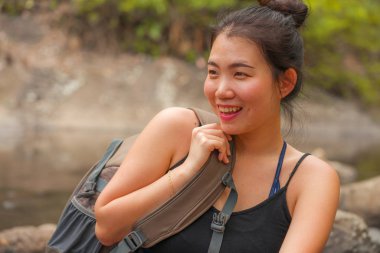 Genç, güzel ve mutlu Asyalı kadın sırt çantasıyla dağları aşarak nehri geçiyor. Tatil doğasının tadını çıkarıyor ve neşeli bir yürüyüş yapıyor. 