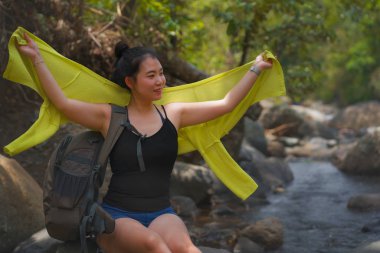 Genç, güzel ve mutlu Asyalı bir Japon kadın sırt çantasıyla dağları aşarak nehri geçiyor. Tatil doğasının tadını çıkarıyor ve neşeli bir yürüyüş yapıyor.