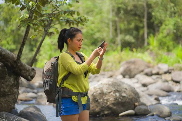 Mujer china asiática feliz llevando mochila trekking en las montañas cruzando río disfrutando de vacaciones naturaleza y ambiente fresco senderismo tomando fotos con teléfono móvil — Foto de Stock