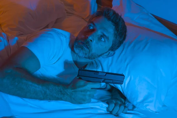 Noční nervózní portrét mladého stresujícího a paranoidního Američana ležícího na posteli a neschopného usnout s pistolí v ruce a rozhlížejícího se vyděšeným pocitem hrozící paranoie — Stock fotografie