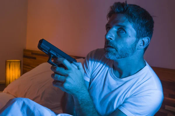 Potret malam yang tegang muda stres dan pria Amerika paranoid duduk di tempat tidur tidak bisa tidur memegang pistol melihat sekitar takut merasa terancam menderita paranoia — Stok Foto