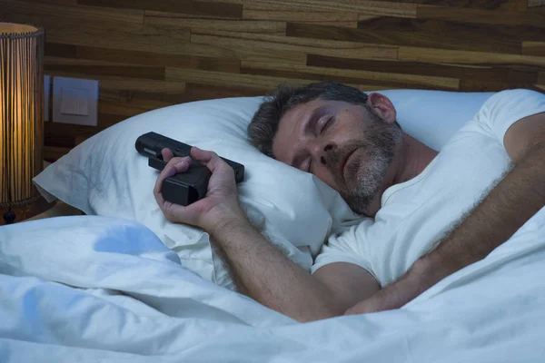 Ritratto notturno di giovane uomo americano stressato e paranoico a letto che dorme e tiene in mano la pistola temendo intrusi che irrompono in casa in paranoia e concetto di autodifesa — Foto Stock