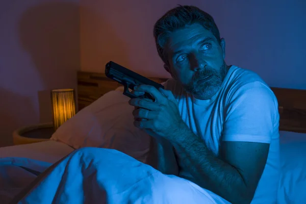 Éjszakai feszült portré fiatal stresszes és paranoiás amerikai férfi feküdt az ágyon, nem tudott aludni kezében fegyvert nézte körül ijedt szenved paranoia várja betolakodók — Stock Fotó
