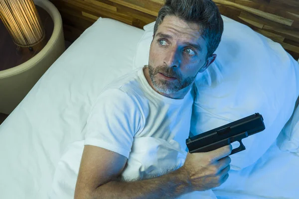 Notte tagliente ritratto di giovane stressato e paranoico uomo americano sdraiato sul letto in grado di dormire pistola in mano guardando intorno paranoia sofferenza paura in attesa intrusi — Foto Stock