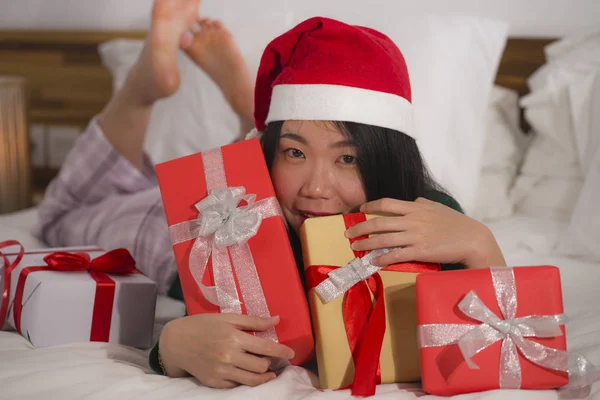 Χριστουγεννιάτικο πορτρέτο του τρόπου ζωής των νέων όμορφη και ευτυχισμένη ασιατική κορεατική γυναίκα στο κρεβάτι στο καπέλο Άγιος Βασίλης κρατώντας πολλά δώρα Χριστούγεννα και κουτιά δώρων ενθουσιασμένοι και χαρούμενα απολαμβάνοντας — Φωτογραφία Αρχείου