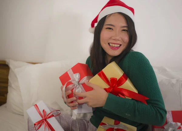Χριστουγεννιάτικο πορτρέτο του τρόπου ζωής των νέων όμορφη και ευτυχισμένη ασιατική κινεζική γυναίκα στο κρεβάτι στο καπέλο Άγιος Βασίλης κρατώντας πολλά δώρα Χριστούγεννα και κουτιά δώρων ενθουσιασμένοι και χαρούμενα — Φωτογραφία Αρχείου