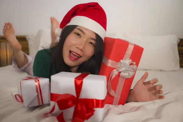 Χριστουγεννιάτικο πορτρέτο του τρόπου ζωής των νέων όμορφη και ευτυχισμένη ασιατική ιαπωνική γυναίκα στο κρεβάτι στο καπέλο Άγιος Βασίλης κρατώντας πολλά δώρα Χριστούγεννα και κουτιά δώρων ενθουσιασμένοι και χαρούμενα — Φωτογραφία Αρχείου