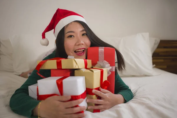 Χριστουγεννιάτικο πορτρέτο του τρόπου ζωής των νέων όμορφη και ευτυχισμένη ασιατική κινεζική γυναίκα στο κρεβάτι στο καπέλο Άγιος Βασίλης κρατώντας πολλά δώρα Χριστούγεννα και κουτιά δώρων ενθουσιασμένοι και χαρούμενα — Φωτογραφία Αρχείου