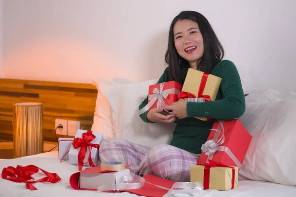 年轻、快乐、甜美的亚洲女人坐在床上准备圣诞礼物、包装礼品盒、加缎带的圣诞生活方式画像 — 图库照片
