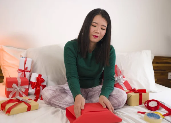 Χριστουγεννιάτικο πορτρέτο του τρόπου ζωής των διακοπών των νέων ευτυχισμένη και γλυκιά ασιατική κορεάτισσα γυναίκα κάθεται στο κρεβάτι προετοιμασία Χριστούγεννα δώρα περιτύλιγμα κουτιά δώρων και προσθέτοντας κορδέλες — Φωτογραφία Αρχείου