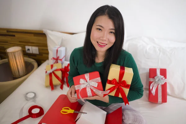 Χριστουγεννιάτικο πορτρέτο του τρόπου ζωής των διακοπών των νέων ευτυχισμένη και γλυκιά ασιατική αμερικανική γυναίκα κάθεται στο κρεβάτι προετοιμασία Χριστούγεννα δώρα περιτύλιγμα κουτιά δώρων και προσθέτοντας κορδέλες — Φωτογραφία Αρχείου
