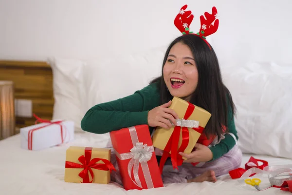 Χριστουγεννιάτικο πορτρέτο του τρόπου ζωής των διακοπών των νέων ευτυχισμένη και όμορφη Ασιατική αμερικανική γυναίκα στο κρεβάτι σε γλυκά κέρατα ταράνδων προετοιμασία Χριστούγεννα παρουσιάζει συσκευασία κουτιά δώρων — Φωτογραφία Αρχείου