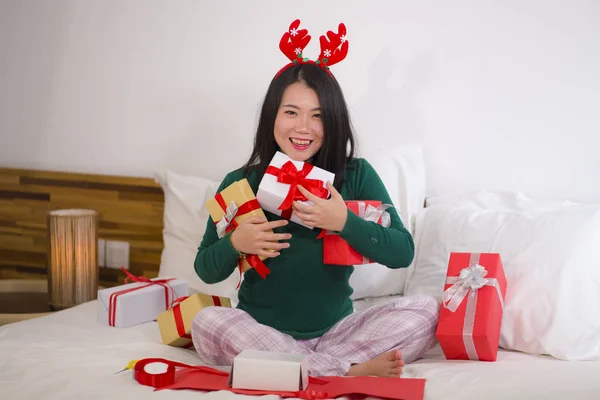 年轻快乐美丽的亚裔韩国女人躺在床上，戴着甜蜜的驯鹿角，准备圣诞礼物，包装礼品盒，享受圣诞佳节 — 图库照片