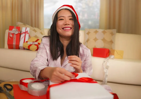 Christmas holidays lifestyle portrait of young beautiful and happy Asian Japanese woman in Santa hat excited wrapping xmas presents packing gifts with paper