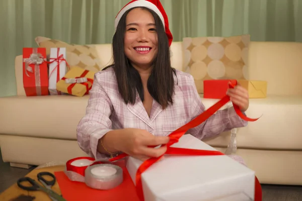 圣诞佳节，身穿圣诞礼帽的年轻、美丽、快乐的亚裔韩裔女子的生活方式画像，兴奋地包装着圣诞礼物，用纸带包裹着 — 图库照片