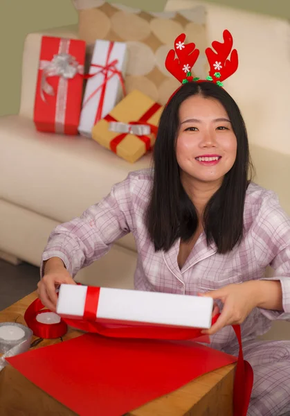 Christmas holidays lifestyle portrait of young beautiful and happy Asian Chinese woman in reindeer horns hat excited wrapping presents packing gifts with paper — 图库照片