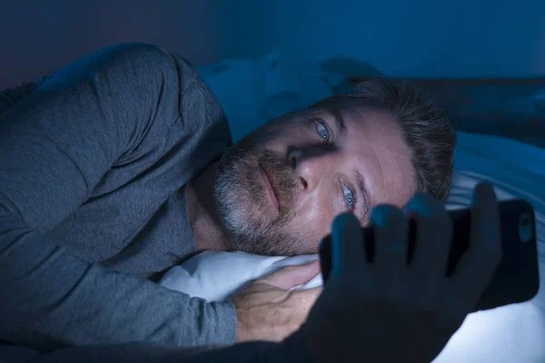 Boldog ember kék szemekkel feküdt az ágyon késő este a sötét fény hálózatépítés mobiltelefon vagy online társkereső mosolygós nyugodt élvezi az internetet a közösségi média függőség — Stock Fotó