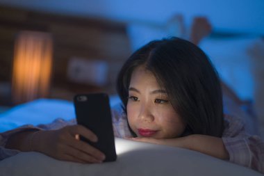 Genç, güzel ve düşünceli, Asyalı, pijamalı bir Çinli kadın. Geceleri internette sosyal medya kullanarak cep telefonuyla rahatlıyor.