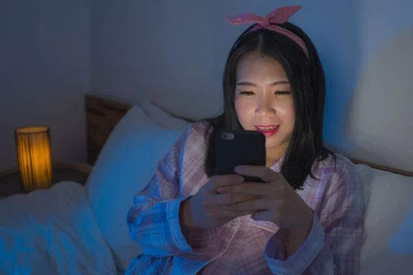 Fiatal szép és boldog édes ázsiai koreai nő íj fejpánt és pizsama hálózatépítés mobiltelefon az ágyban éjszaka ellenőrzése internetes közösségi média app — Stock Fotó