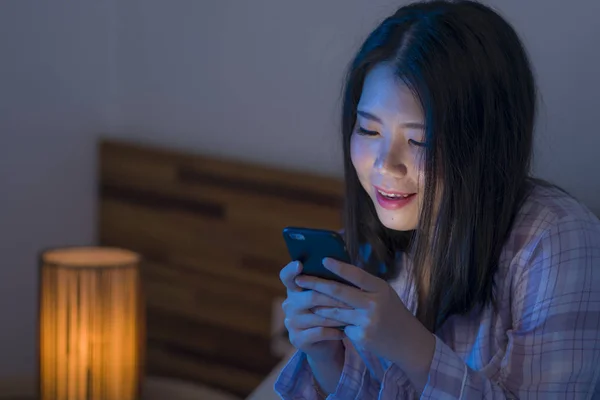 Genç, güzel ve mutlu bir Asyalı kadın pijamalı, cep telefonu uygulaması ile geceleri yatakta eğlenen internet sosyal medya bağımlılığı kavramı. — Stok fotoğraf