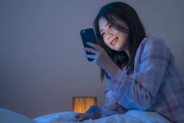 Joven hermosa y feliz dulce mujer coreana asiática con en pijamas disfrutando con aplicación de teléfono móvil en la cama por la noche en internet concepto de adicción a las redes sociales — Foto de Stock