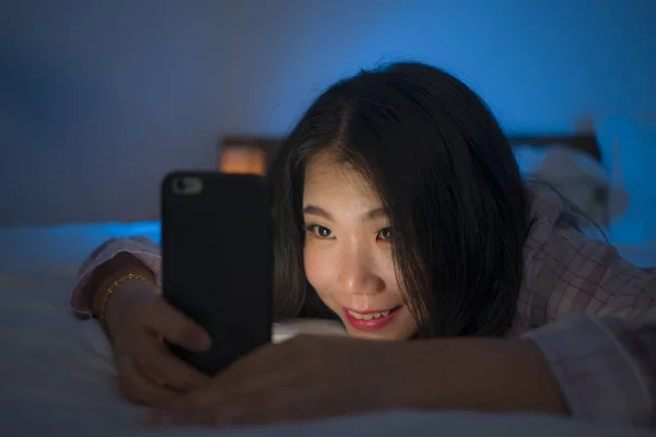 Young beautiful and happy sweet Asian Korean woman with in pajamas enjoying with mobile phone app in bed at night in internet social media addiction concept — 스톡 사진