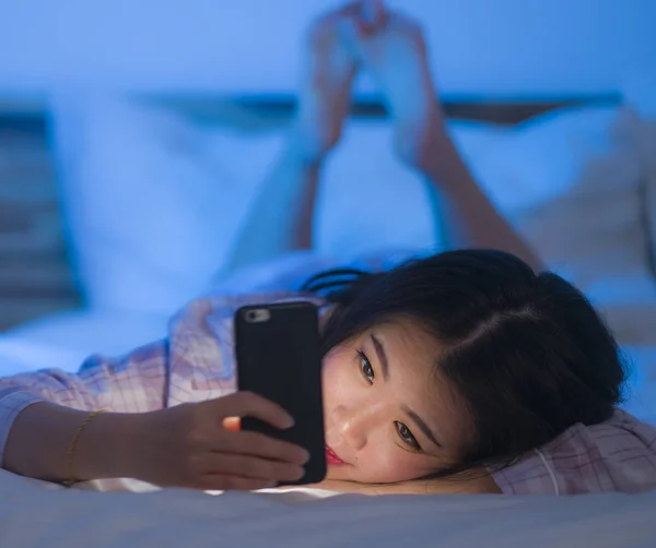 Jong mooi en gelukkig zoet aziatisch koreaans vrouw met in pyjama genieten met mobiele telefoon app in bed 's nachts in internet social media verslaving concept — Stockfoto