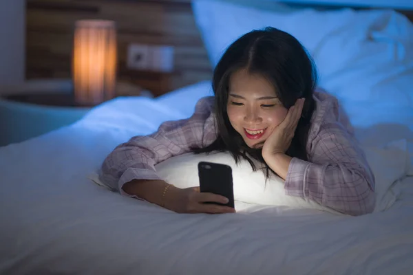 Joven hermosa y feliz dulce mujer coreana asiática con en pijamas disfrutando con aplicación de teléfono móvil en la cama por la noche en internet concepto de adicción a las redes sociales — Foto de Stock