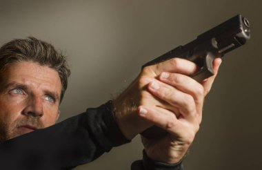 Çekici tetikçi ya da özel ajan elinde silahla karanlık arka planda Hollywood tarzı bir filmde izole edilmiş bir silah tutuyor.