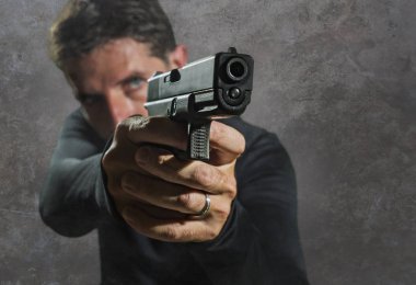 Ciddi ve çekici bir tetikçinin ya da özel bir ajanın karanlık arka planda izole edilmiş silahı tutan resminin derinliği.