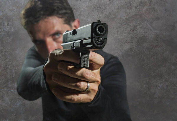 shallow depth of focus action portrait of serious and attractive hitman or special agent man holding gun pointing the weapon isolated on dark background