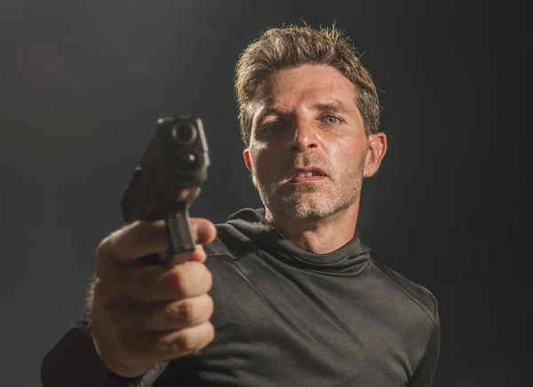 Furioso y atractivo sicario o agente especial hombre sosteniendo pistola apuntando el arma aislada en el fondo oscuro en el servicio secreto de Hollywood película de estilo — Foto de Stock