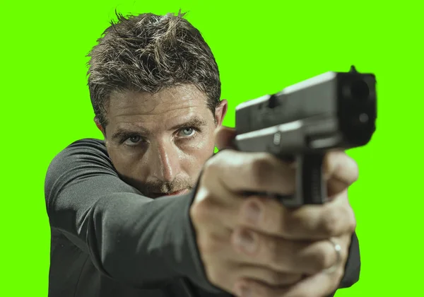 Croma clave verde fondo acción retrato de sicario serio y atractivo o agente especial hombre sosteniendo pistola apuntando la pistola en la luz cinematográfica en el estilo de película servicio secreto — Foto de Stock