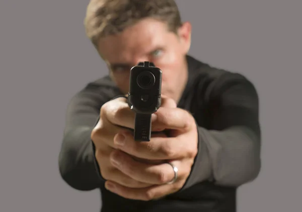 Shallow depth of focus action portrait of serious and attractive hitman or special agent man holding gun pointing the handgun to the camera isolated on dark background — Stock Photo, Image