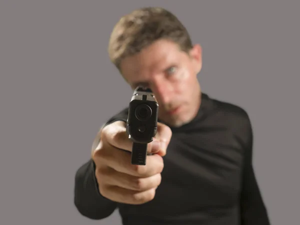 Shallow depth of focus action portrait of serious and attractive hitman or special agent man holding gun pointing the handgun to the camera isolated on dark background — Stock Photo, Image