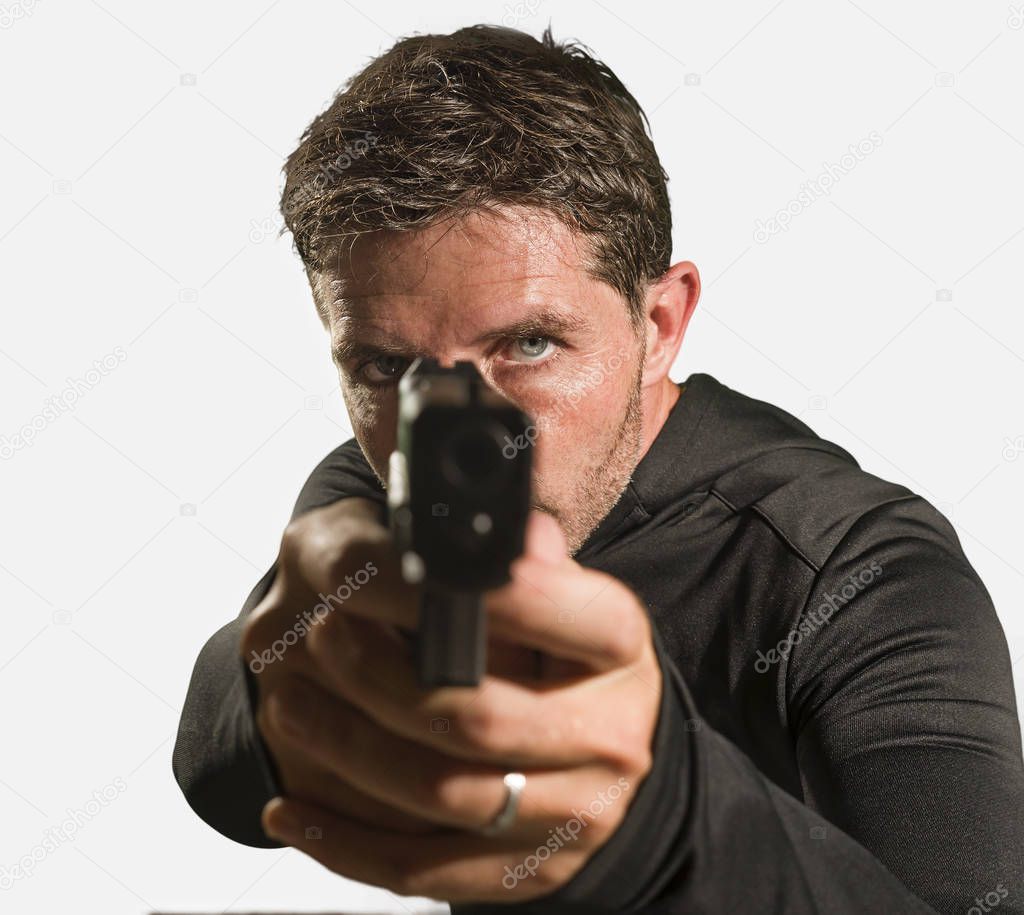  action portrait of serious and attractive hitman or special agent man holding gun pointing the handgun to the camera in Hollywood style movie isolated on studio background