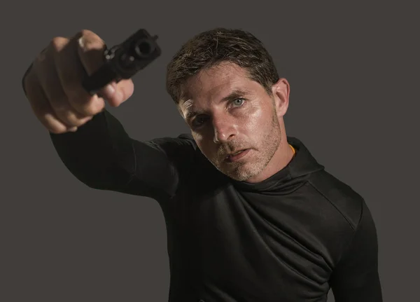 Action-Porträt des wütenden und attraktiven Hitman oder Special Agent Mann mit Pistole zeigt die Handfeuerwaffe auf Kamera isoliert auf dunklem Hintergrund in Geheimdienst-Film-Stil — Stockfoto