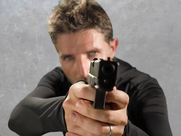 Портрет дії злий і привабливий хітмен або спеціальний агент, який тримає зброю, вказуючи пістолет на камеру ізольовано на студійному фоні в стилі таємного сервісу — стокове фото