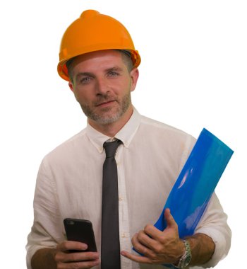 corporate portrait of attractive and successful industrial engineer or contractor man in working hardhat smiling happy holding mobile phone and folder