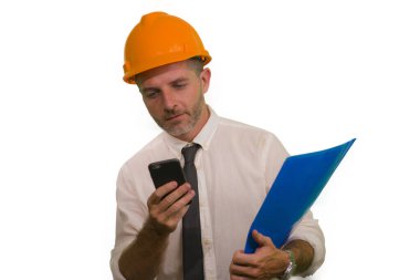 corporate portrait of attractive and successful industrial engineer or contractor man in working hardhat smiling happy holding mobile phone and folder