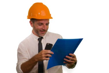corporate portrait of attractive and successful industrial engineer or contractor man in working hardhat smiling happy holding mobile phone and folder