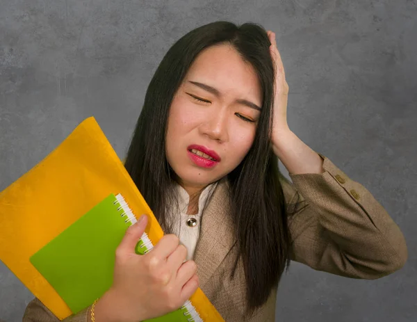 corporate business stress portrait of young attractive upset and stressed executive Asian Chinese woman tired and unhappy holding paperwork overwhelmed