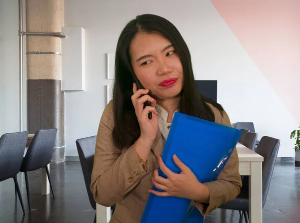 corporate business stress portrait of young attractive and stressed executive Asian Chinese woman tired and unhappy talking on mobile phone holding paperwork overwhelmed