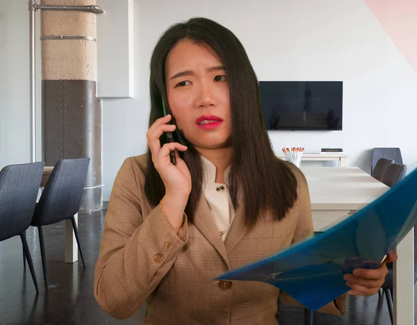 corporate business stress portrait of young attractive and stressed executive Asian Korean woman tired and unhappy talking on mobile phone holding paperwork overwhelmed