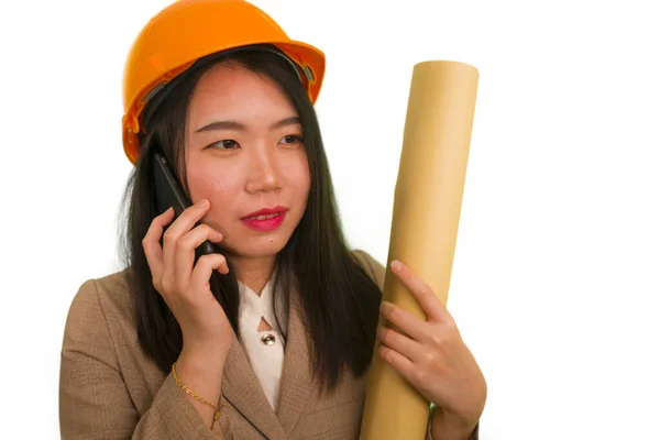 Mooi en gelukkig aziatisch koreaans vrouw in hardhat holding gebouw blauwdrukken als architect ingenieur of bouwheer supervisor praten op mobiele telefoon — Stockfoto
