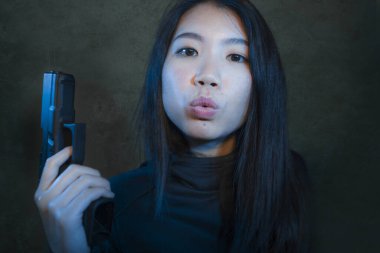 Tabancalı Asyalı bir kız. Çekici ve tehlikeli görünümlü bir Koreli kadının dramatik portresi. Elinde silah var.