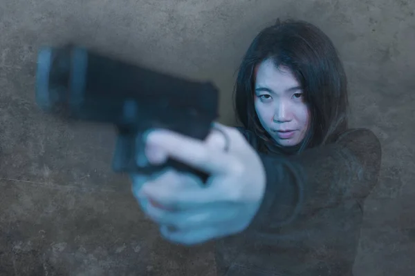 Chica asiática apuntando pistola - dramático retrato de acción de joven atractivo y peligroso buscando mujer china sosteniendo pistola disparando en fondo grunge oscuro —  Fotos de Stock