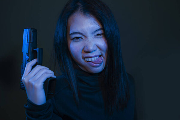 Asian girl with handgun - dramatic portrait of young attractive and dangerous looking Chinese woman holding gun posing playful dark grunge background and cinematic style